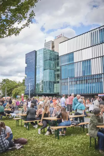 Menschengruppen sitzen Draußen vor der Rhein-Mosel-Halle